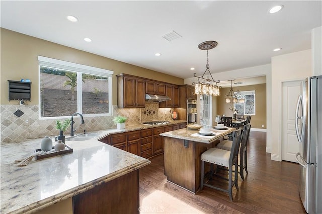 kitchen with sink, hanging light fixtures, a kitchen bar, stainless steel appliances, and a kitchen island