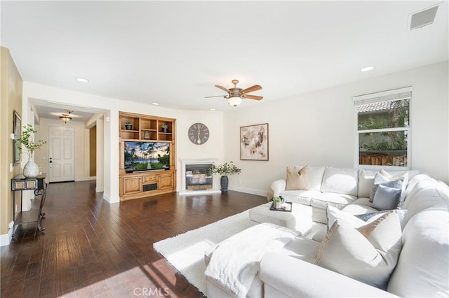 living room with built in shelves, dark hardwood / wood-style floors, and ceiling fan