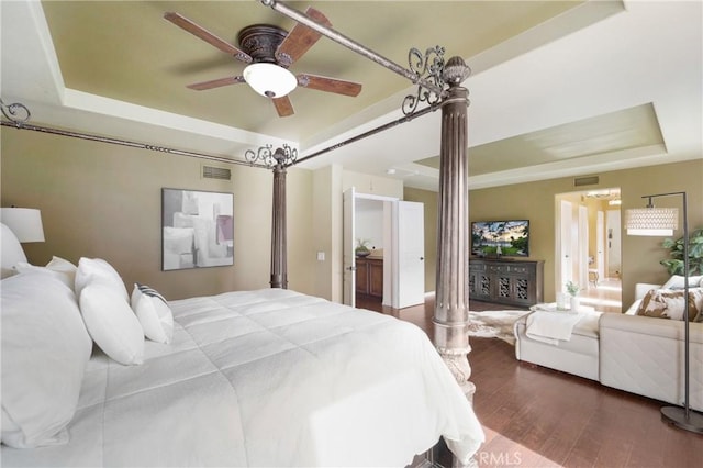 bedroom featuring dark wood-type flooring, decorative columns, a raised ceiling, and ceiling fan