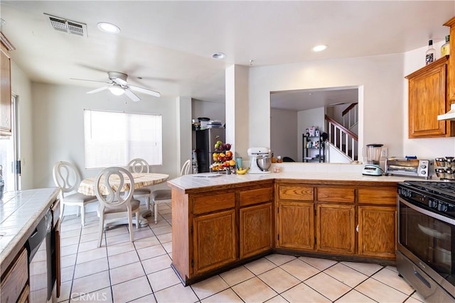 kitchen with tile countertops, stainless steel gas range, light tile patterned floors, and kitchen peninsula