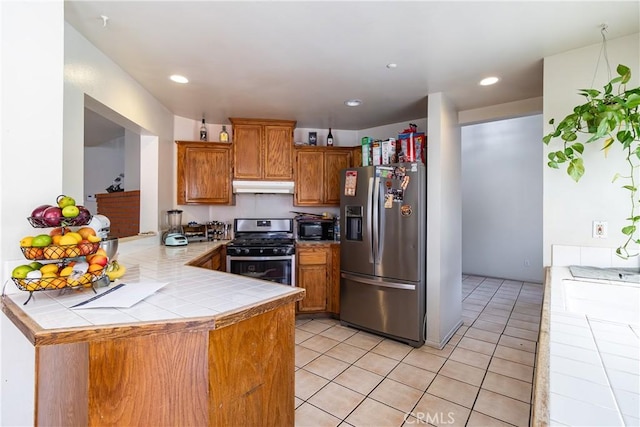 kitchen featuring light tile patterned floors, tile countertops, kitchen peninsula, and appliances with stainless steel finishes