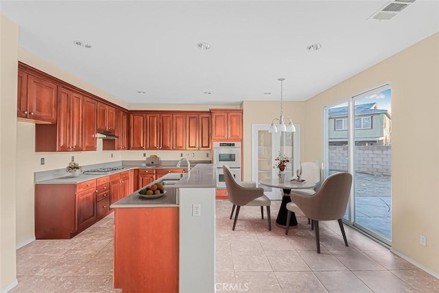 kitchen featuring decorative light fixtures, an island with sink, sink, light tile patterned floors, and stainless steel appliances