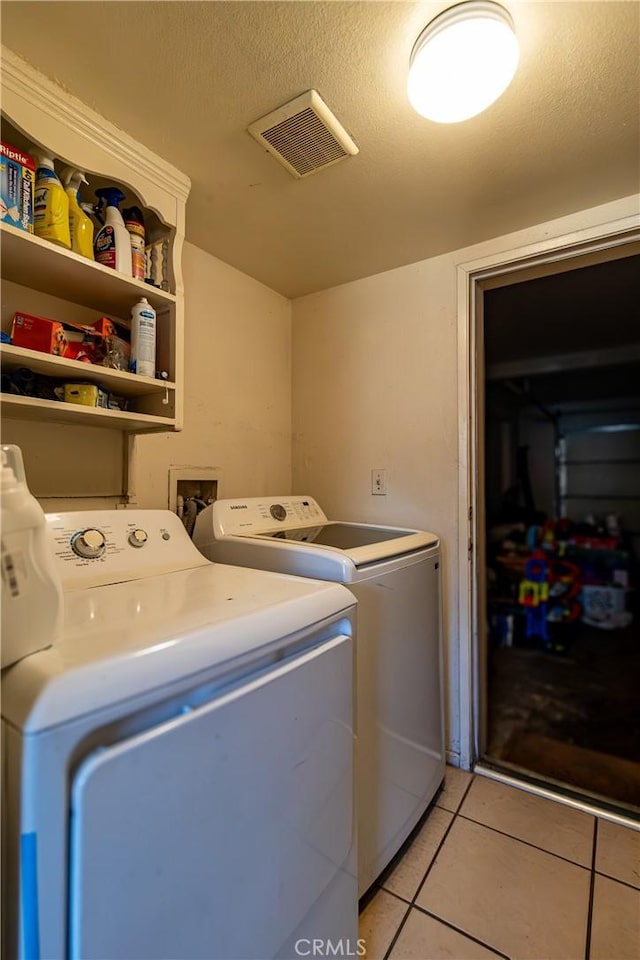 washroom with washer and dryer, light tile patterned floors, and a textured ceiling