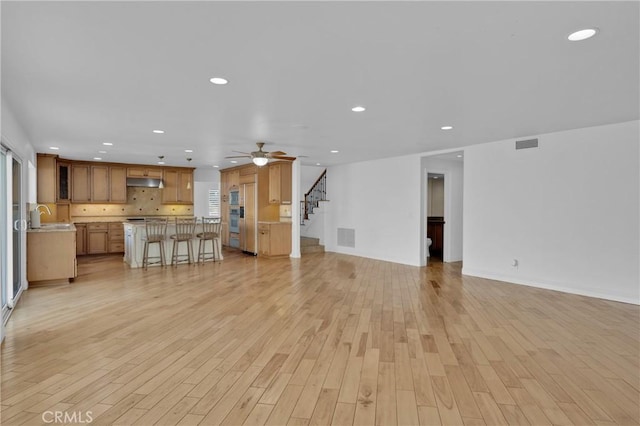 unfurnished living room with ceiling fan, sink, and light hardwood / wood-style flooring