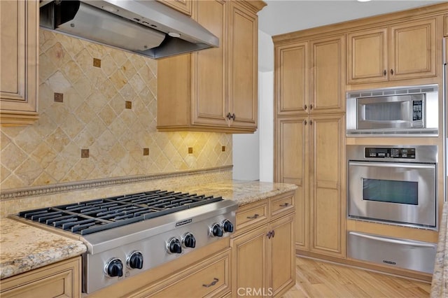 kitchen with tasteful backsplash, light wood-type flooring, light stone countertops, stainless steel appliances, and range hood