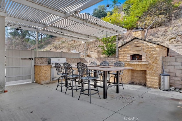 view of patio / terrace with a bar, a pergola, an outdoor stone fireplace, and an outdoor kitchen
