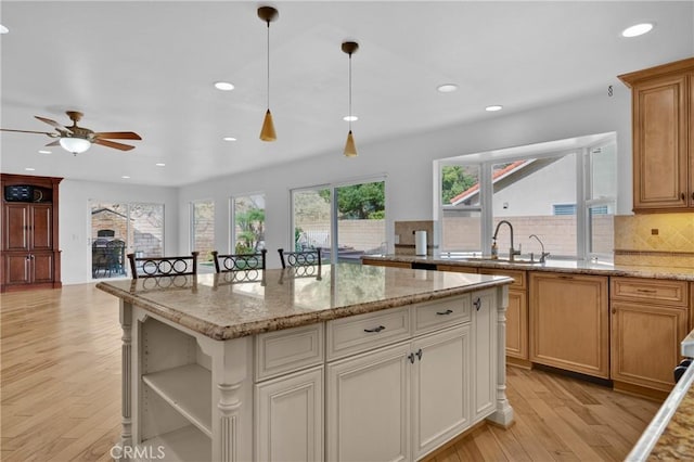 kitchen with sink, hanging light fixtures, a center island, light hardwood / wood-style floors, and light stone countertops