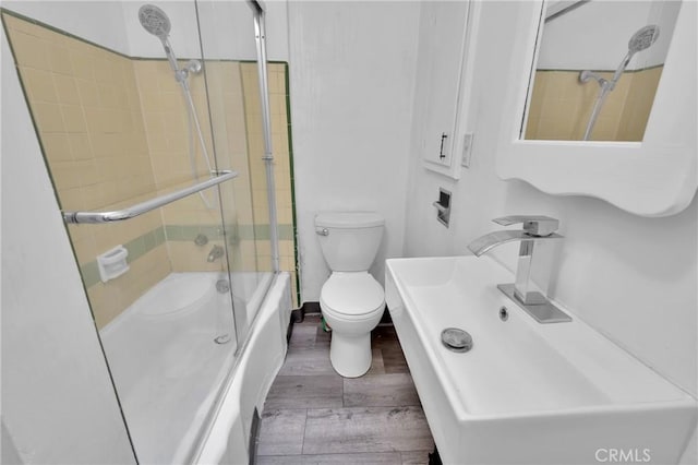 full bathroom with sink, wood-type flooring, combined bath / shower with glass door, and toilet