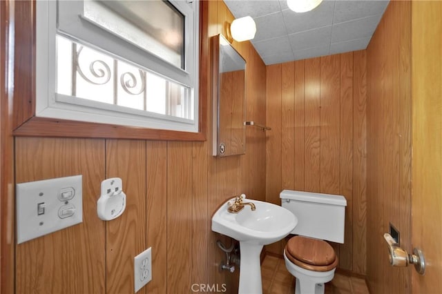 bathroom with tile patterned flooring, wood walls, and toilet