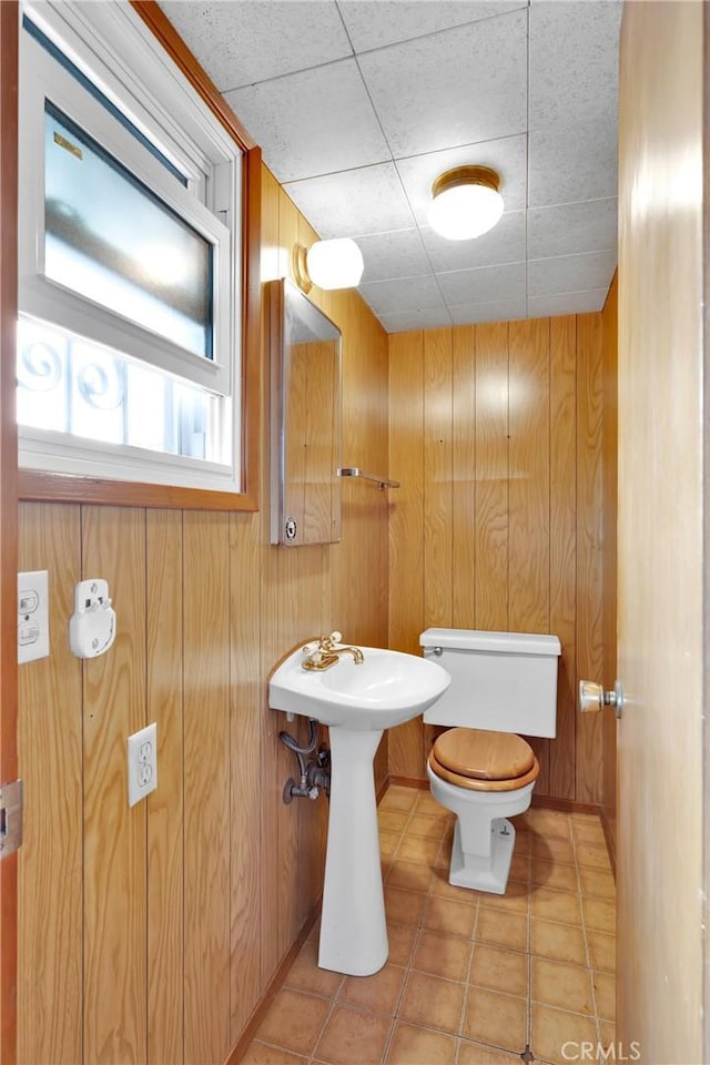 bathroom with tile patterned flooring, wooden walls, and toilet