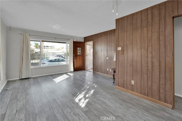 interior space with wood walls, a textured ceiling, and light hardwood / wood-style flooring