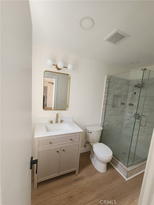 bathroom featuring hardwood / wood-style flooring, vanity, a shower with door, and toilet