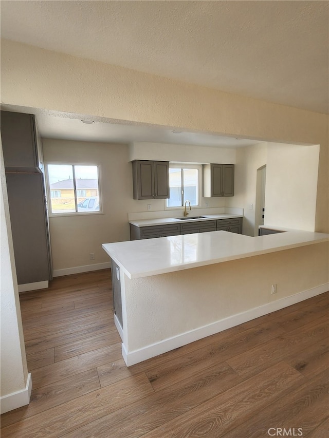 kitchen featuring sink, gray cabinetry, light hardwood / wood-style floors, kitchen peninsula, and a textured ceiling