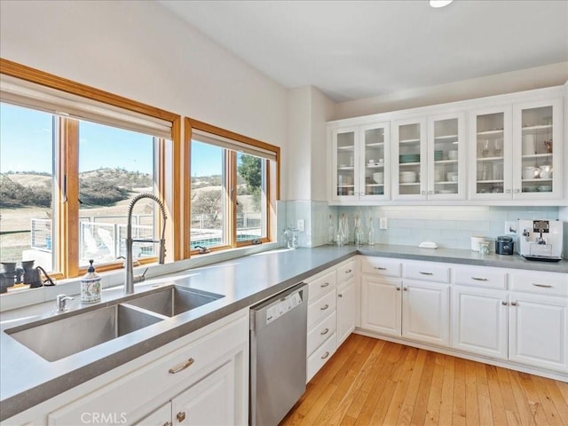 kitchen featuring a sink, white cabinets, stainless steel dishwasher, decorative backsplash, and glass insert cabinets