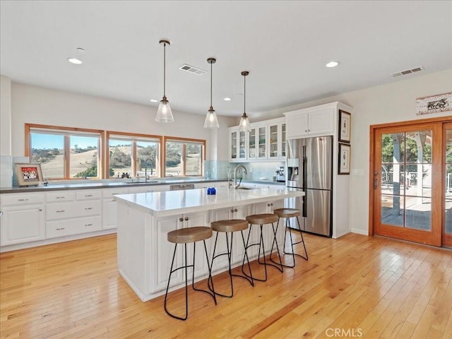 kitchen featuring light countertops, glass insert cabinets, white cabinets, an island with sink, and stainless steel fridge with ice dispenser