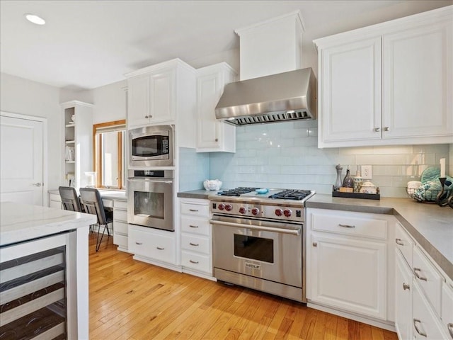 kitchen with wine cooler, appliances with stainless steel finishes, light countertops, wall chimney range hood, and white cabinetry