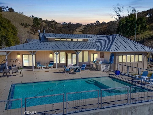 back of property at dusk featuring metal roof, exterior kitchen, a standing seam roof, and board and batten siding