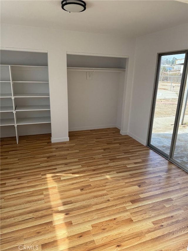 unfurnished bedroom with access to exterior, light hardwood / wood-style flooring, and multiple closets