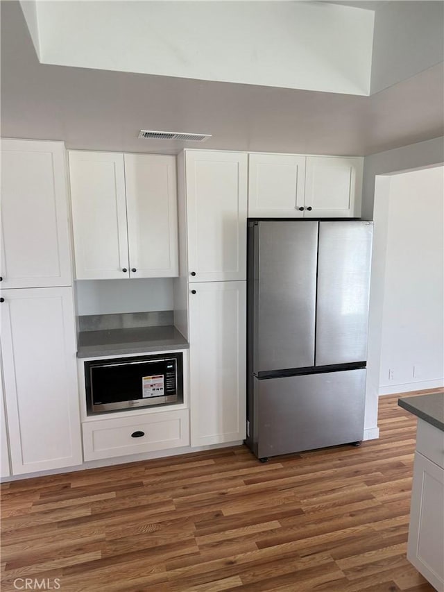 kitchen featuring built in microwave, dark wood-type flooring, stainless steel refrigerator, and white cabinets