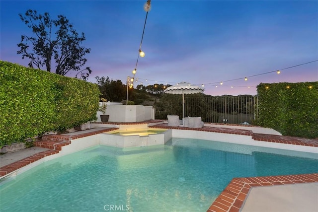 pool at dusk with an in ground hot tub