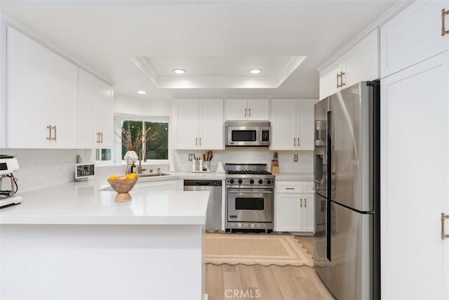 kitchen featuring a raised ceiling, appliances with stainless steel finishes, white cabinets, and kitchen peninsula