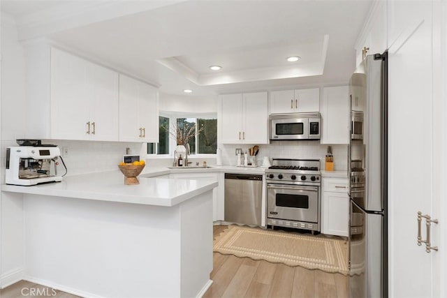 kitchen with a raised ceiling, white cabinets, backsplash, kitchen peninsula, and stainless steel appliances