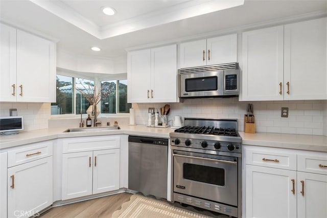 kitchen featuring appliances with stainless steel finishes, white cabinetry, sink, a tray ceiling, and light wood-type flooring