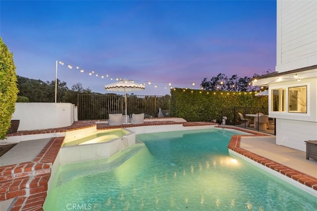 pool at dusk featuring an in ground hot tub and a patio