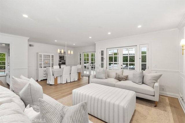 living room featuring light hardwood / wood-style flooring, ornamental molding, french doors, and a chandelier