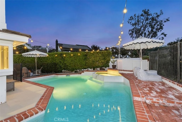 pool at dusk with an in ground hot tub and a patio area