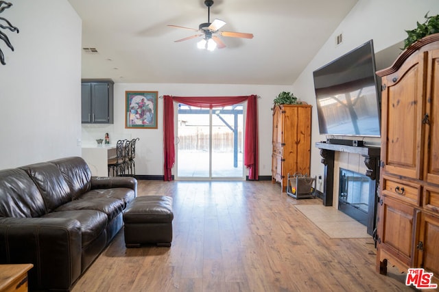 living room with lofted ceiling, a tiled fireplace, ceiling fan, and light wood-type flooring