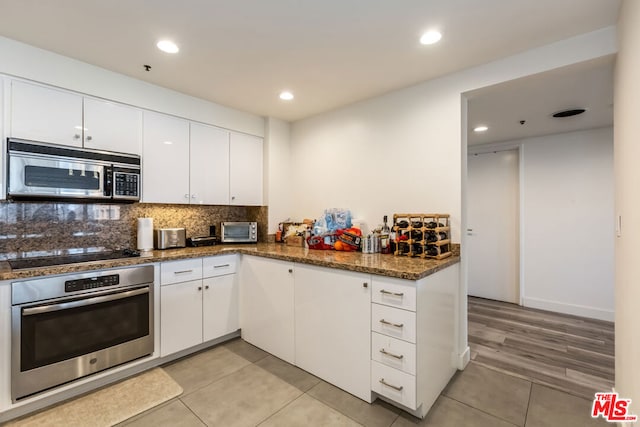 kitchen featuring light tile patterned flooring, appliances with stainless steel finishes, dark stone countertops, white cabinets, and decorative backsplash