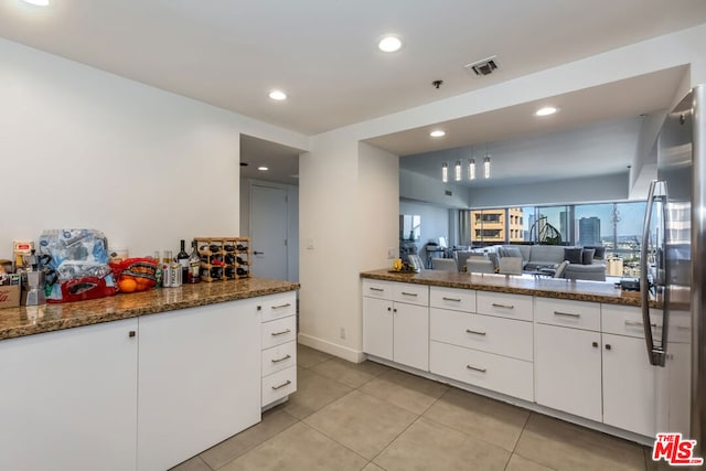 kitchen featuring dark stone countertops, stainless steel refrigerator, white cabinets, and light tile patterned flooring