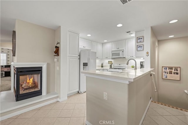 kitchen with light tile patterned floors, white appliances, a multi sided fireplace, white cabinets, and kitchen peninsula