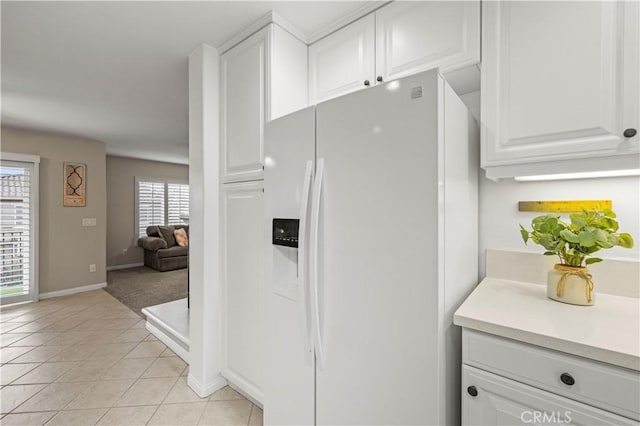 kitchen with light tile patterned floors, light countertops, white cabinetry, white fridge with ice dispenser, and baseboards