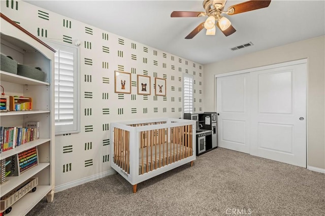 bedroom featuring a nursery area, carpet flooring, ceiling fan, and a closet