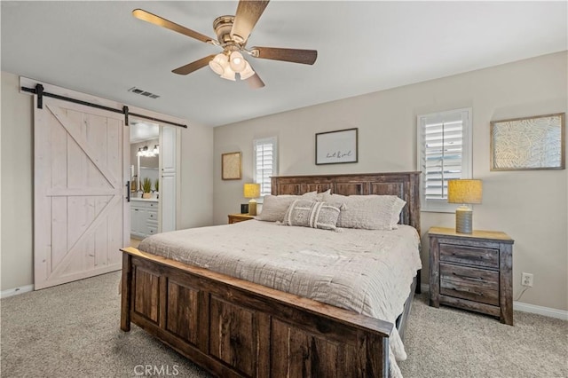 carpeted bedroom with ensuite bath, a barn door, and ceiling fan