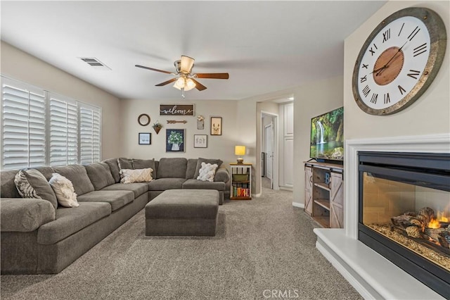 living area with carpet, a glass covered fireplace, a ceiling fan, and baseboards