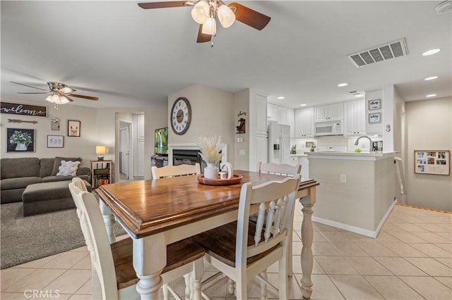 dining space with light tile patterned floors, visible vents, a ceiling fan, a fireplace, and recessed lighting