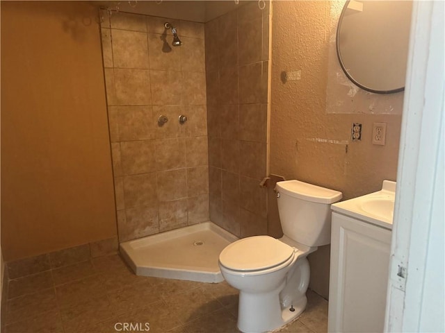 bathroom with tile patterned floors, vanity, toilet, and a tile shower