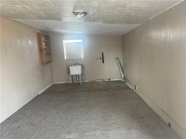 basement featuring dark colored carpet, sink, a textured ceiling, and wood walls