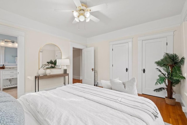 bedroom with multiple closets, ensuite bath, ceiling fan, and hardwood / wood-style floors