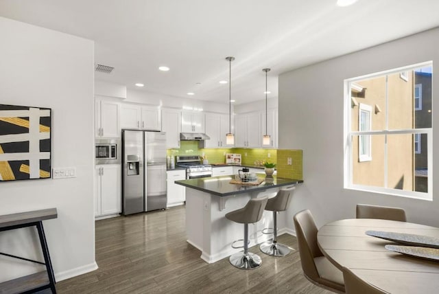 kitchen featuring appliances with stainless steel finishes, pendant lighting, white cabinets, a kitchen breakfast bar, and kitchen peninsula