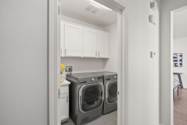 washroom with light tile patterned flooring, cabinets, and washer and dryer