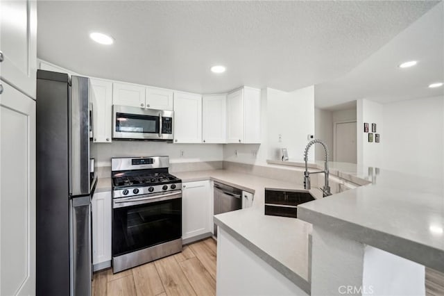 kitchen with sink, white cabinetry, light hardwood / wood-style flooring, kitchen peninsula, and stainless steel appliances