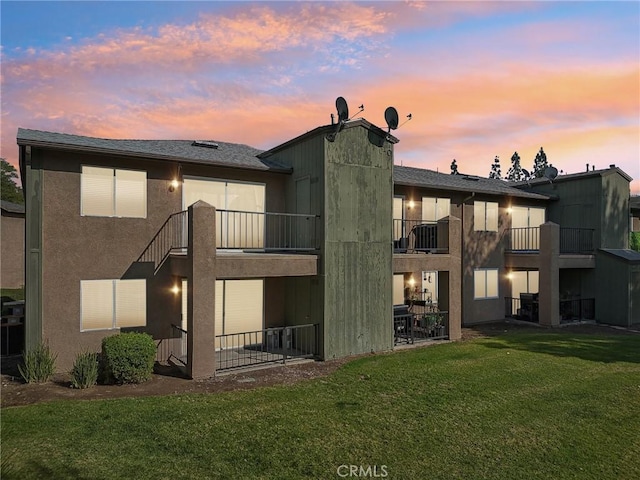 back house at dusk featuring a lawn and a balcony