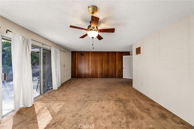 spare room with ceiling fan, carpet flooring, a textured ceiling, and wooden walls