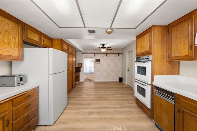 kitchen with white appliances, tile counters, ceiling fan, and light wood-type flooring