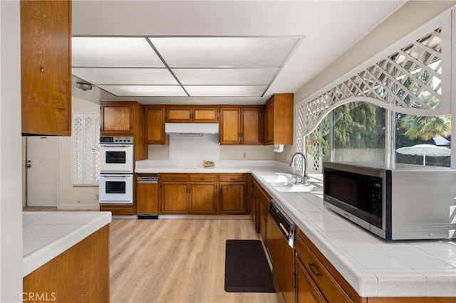 kitchen featuring sink, light hardwood / wood-style flooring, tile counters, black dishwasher, and double oven