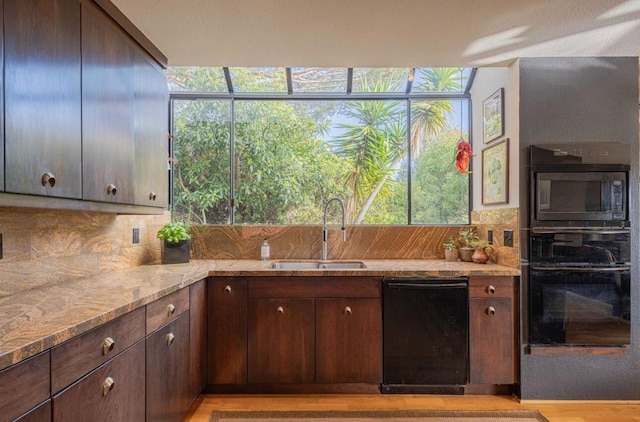 kitchen featuring sink, decorative backsplash, light stone counters, black appliances, and dark brown cabinets